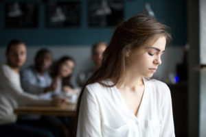 Sad woman contemplating an age discrimination lawsuit while people ridicule her in the background.