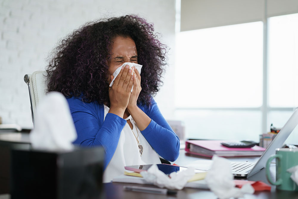 woman sneezing at desk, rights to paid time off during coronavirus