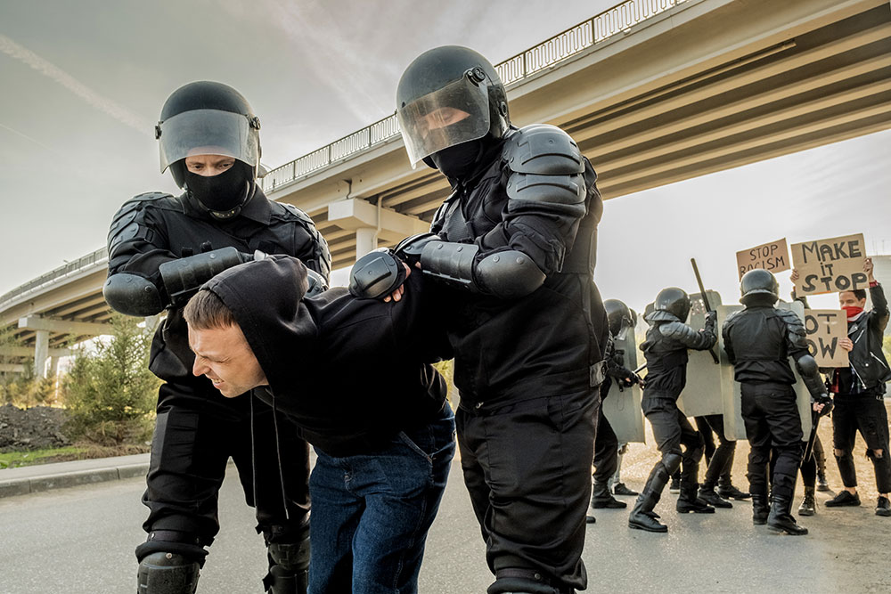 Two police officers physically detaining a man at a protest. This could be an example of police misconduct.